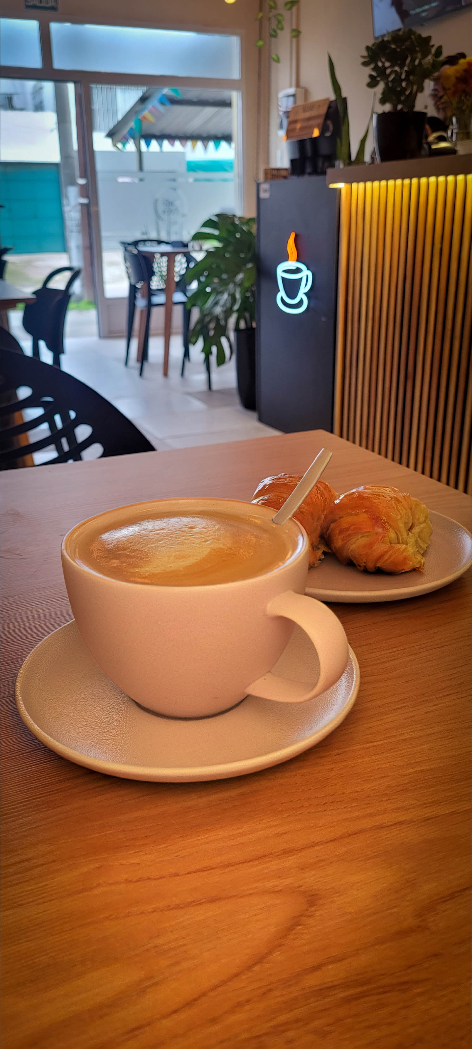 Café cremoso en taza con medialunas doradas en la mesa de madera