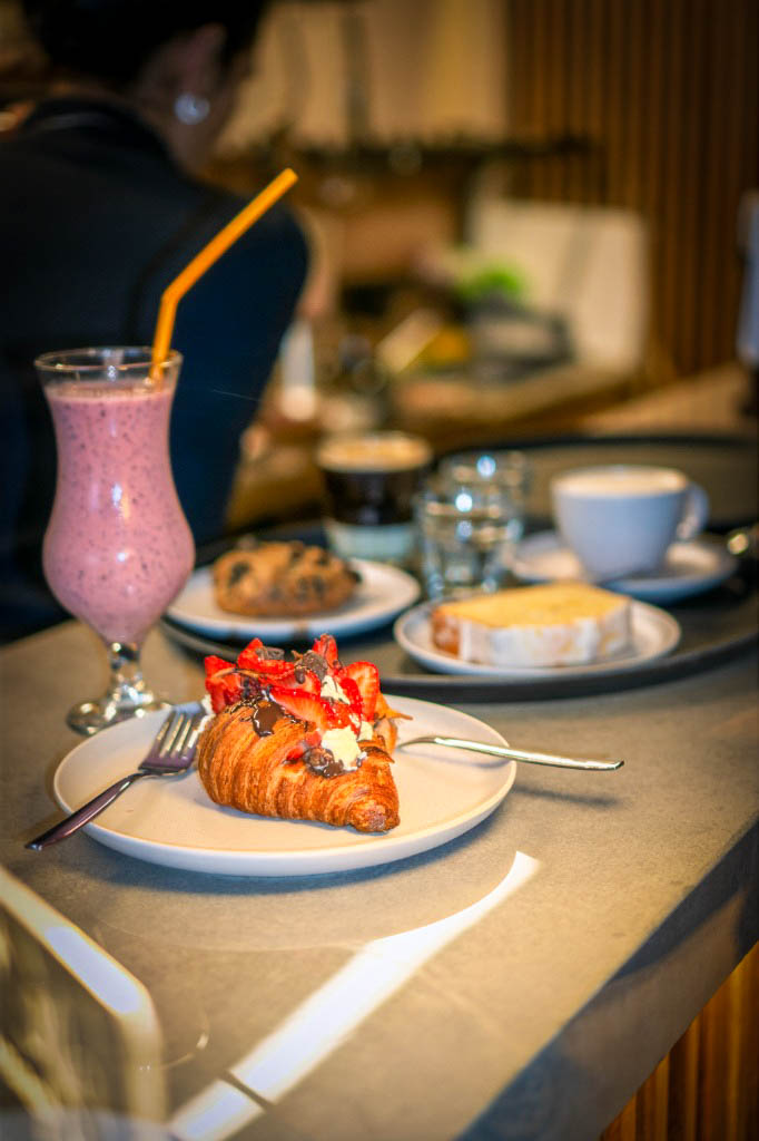 Croissant artesanal relleno con crema y frutillas, acompañado de licuado y café